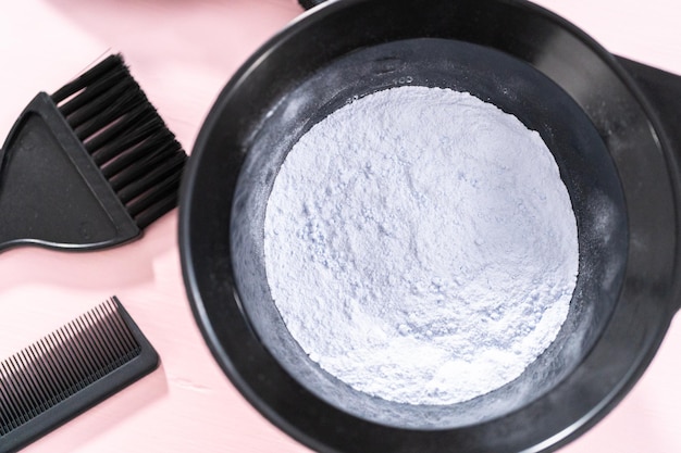 hair color dye powder in a black plastic mixing bowl on a pink background.