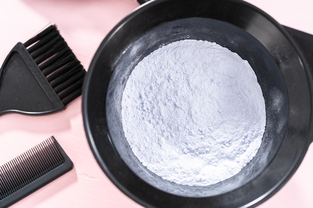 Hair color dye powder in a black plastic mixing bowl on a pink background.