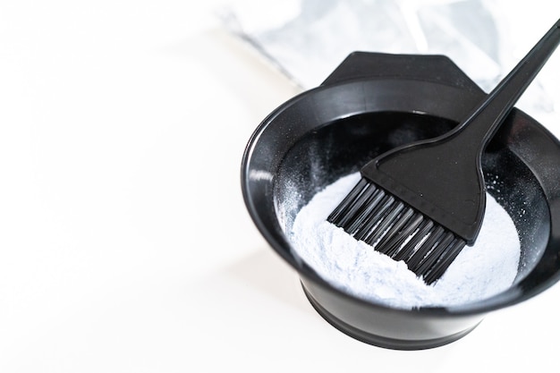 Hair color dye powder in a black plastic mixing bowl on a white background.