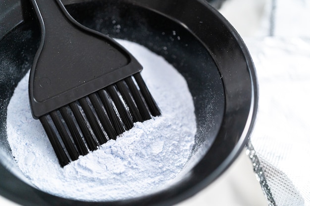 Hair color dye powder in a black plastic mixing bowl on a white background.