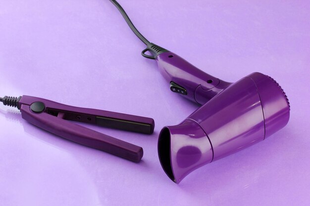 Hair dryer and straighteners on purple background