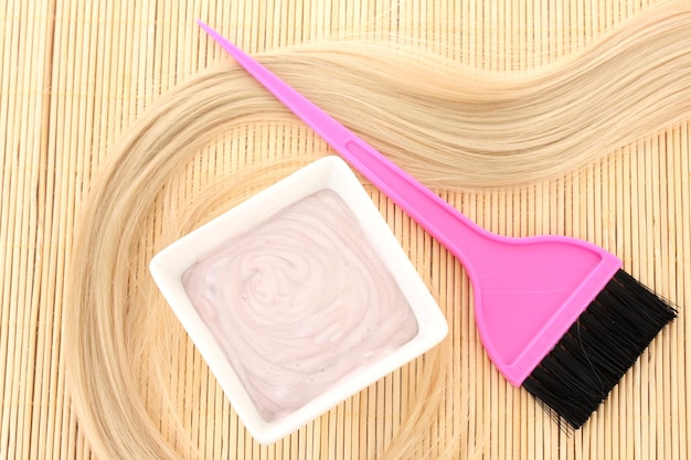 Photo hair dye in bowl and brush for hair coloring on beige bamboo mat closeup