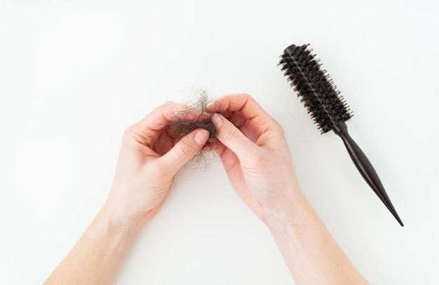 Perdita di capelli nel pettine, problema quotidiano di perdita di capelli grave, su sfondo bianco. la ragazza tiene tra le mani i capelli caduti.