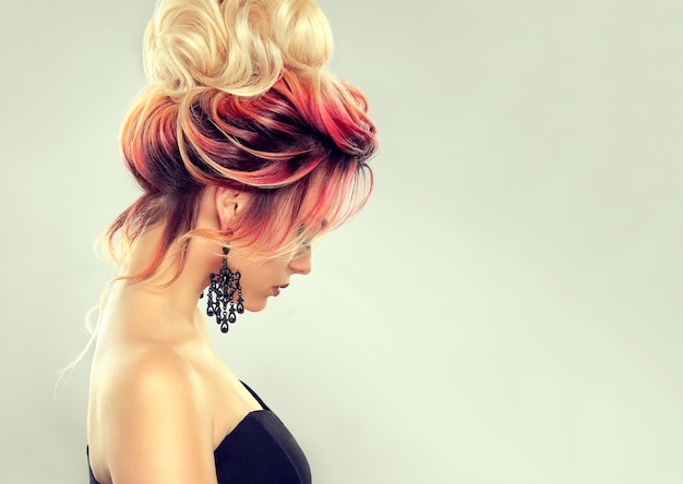 Hair painting. Young attractive woman with multi colored hair gathered in elegant evening hairstyle with big blonde bun. Hairdressing art and coloration of hair. 