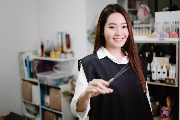 Hair salon concept a pretty hairdresser posing with scissers in a hand  in her hair salon surrounded by haircare products and equipment.