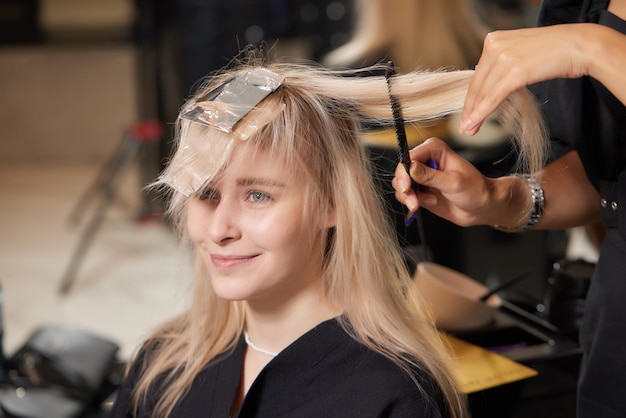 Hair stylist makes bouffant using comb on thin strands Shatush technique for hair lightening