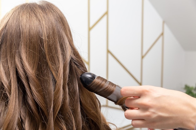 Hair stylist prepares woman makes curls hairstyle with curling iron