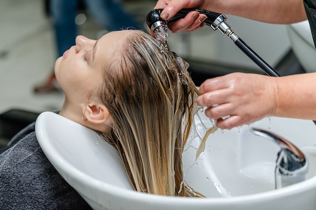 Hair stylist washing hair of a young pretty woman in a beauty salon.