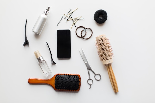 Фото Инструменты для волос, концепция красоты и парикмахерской - смартфон, ножницы, щетки и стилистические спреи с булавками и галстуками на белом фоне