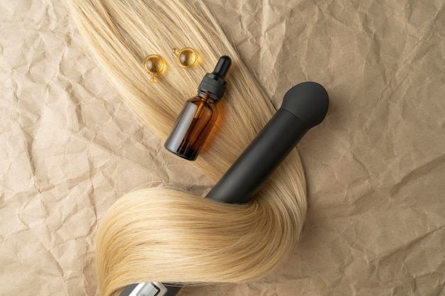 A hair treatment essential oil for smoothing hair and a hair curling styler lying on a brown craft paper background