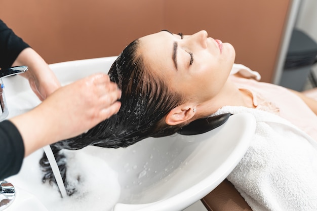 Foto trattamento per capelli. felice giovane donna appoggiata al lavandino mentre si lava i capelli. concetto di bellezza