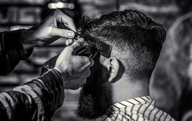 Foto concetto di taglio di capelli uomo che visita parrucchiere in barbiere barbiere lavora con tagliacapelli cliente hipster che ottiene taglio di capelli in bianco e nero