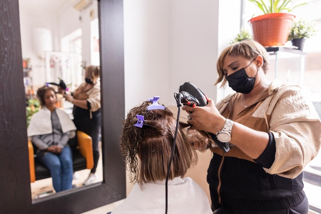 Foto taglio di capelli acconciatura ispanica salone di bellezza professionale femminile con maschera facciale coronavirus razza mista