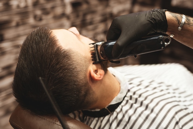 Стрижка головы в парикмахерской, парикмахер стрижет волосы на голове клиента.