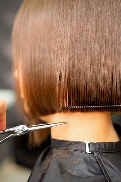 Taglio di capelli di capelli corti di giovane donna bianca per mano di un parrucchiere in un parrucchiere vista posteriore da vicino