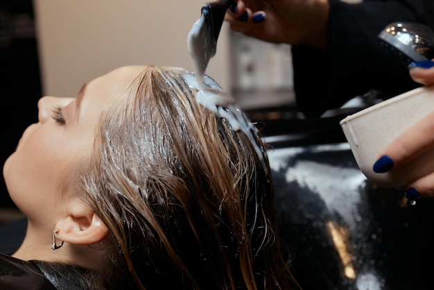 Hairdresser in beauty salon washes his client hair before procedure of applying natural restoring in...