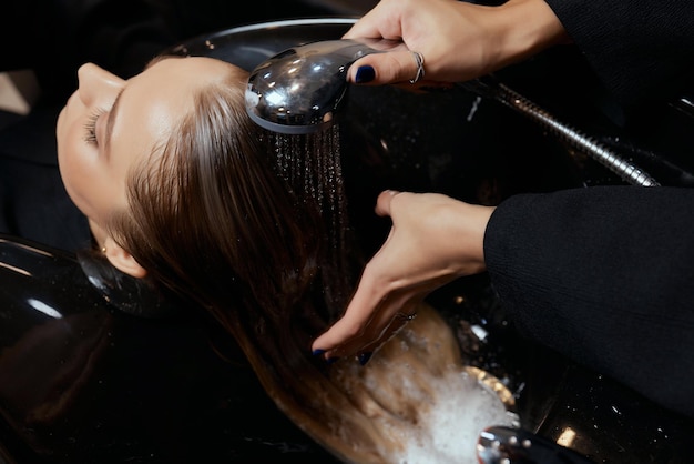 Hairdresser in beauty salon washes his client hair before procedure of applying natural restoring in...