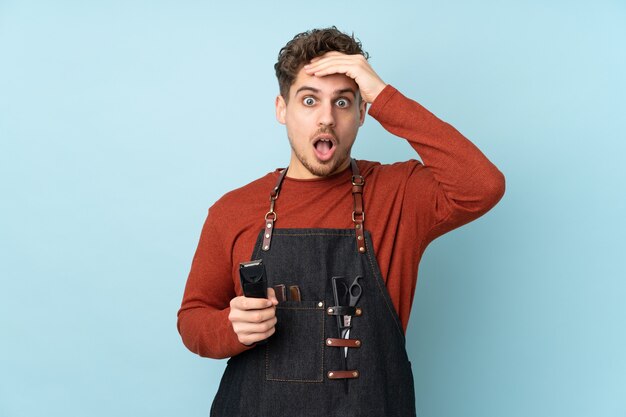 Uomo caucasico del parrucchiere isolato sull'azzurro con l'espressione facciale di sorpresa