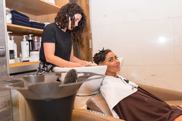 Hairdresser cleaning the head with hot water and soap to a brunette client