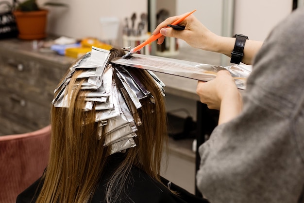 Foto parrucchiere che colora i capelli della donna del cliente nel concetto della tintura professionale del salone di bellezza del barbiere dello studio