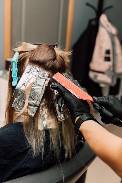 Hairdresser combing a strand of dyed blonde hair with a comb