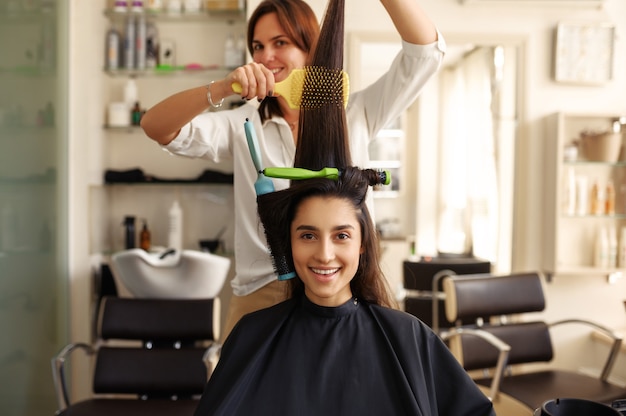 Parrucchiere arriccia e pettina i capelli della donna, parrucchiere. stilista e cliente in parrucchiere. affari di bellezza, servizio professionale