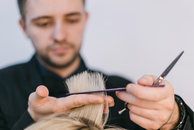 парикмахер стрижет прядь белых волос женщины в парикмахерской. Крупный план