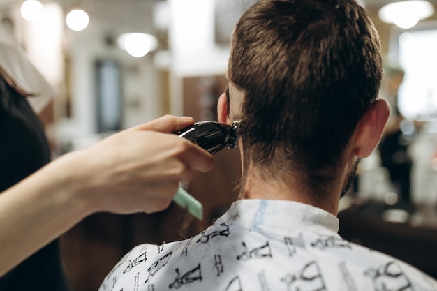 Un parrucchiere taglia un giovane ragazzo con un tagliacapelli pettinandosi i capelli in testa opera del maestro nel taglio di capelli da uomo in un barbiere