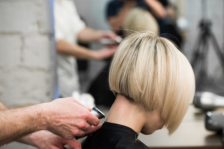 Hairdresser cutting client's hair in salon with electric razor closeup.