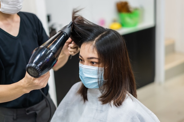 Photo hairdresser cutting the hair to female client wearing medical mask to protection coronavirus