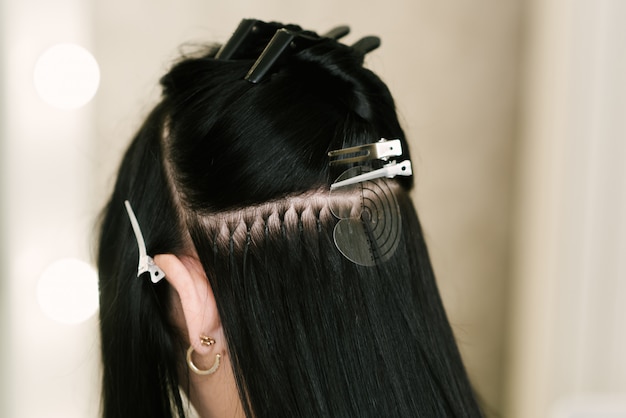 The hairdresser does hair extensions to a young girl in a\
beauty salon. professional hair care. close up of capsules and\
strands of grown hair