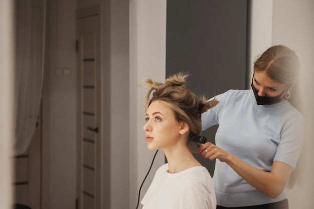 Hairdresser does hairstyle cute pretty young woman in beauty salon. Customer service in interior room create an amazing image. Work hairstyles creation wizard. Concept style, satisfaction. Copy space