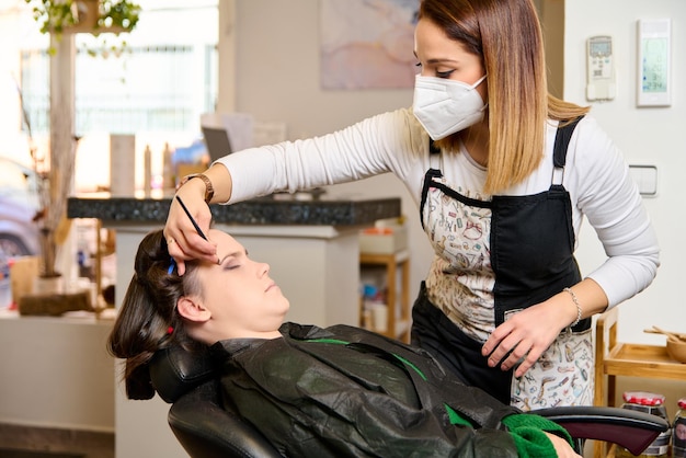 Parrucchiere che fa il trucco e lo styling di una giovane cliente femminile in un salone di bellezza