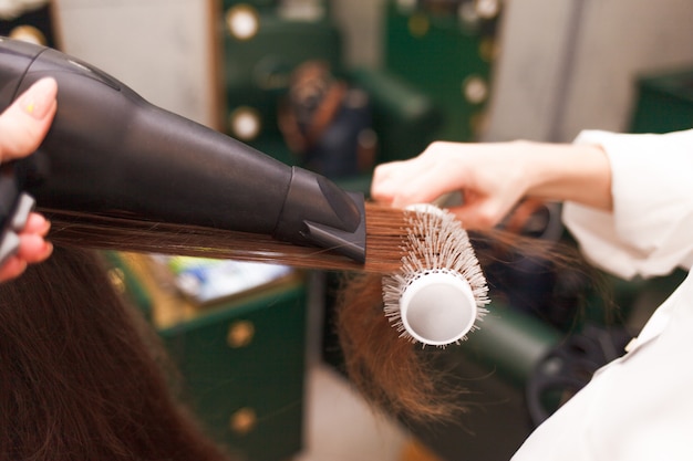 Парикмахер сушит волосы клиента с феном и расческой. Женщина в салоне красоты