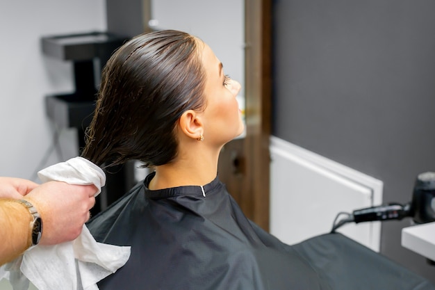 The hairdresser dries the washed hair with a towel to a beautiful young brunette woman at a beauty salon