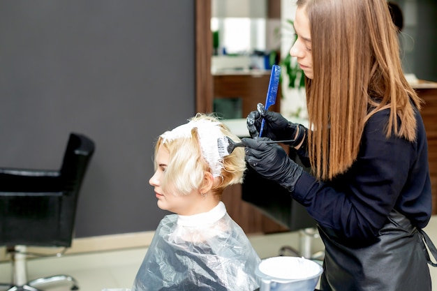 Hairdresser dyes hair of woman.