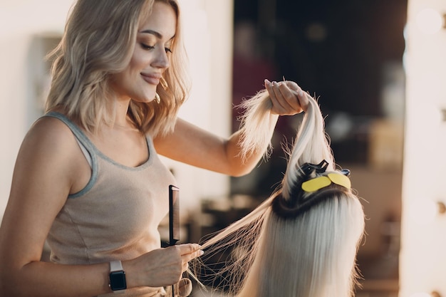 写真 美容院のプロのヘアエクステンションでブロンドの髪を持つ若い女性にヘアエクステンションを作る美容師の女性