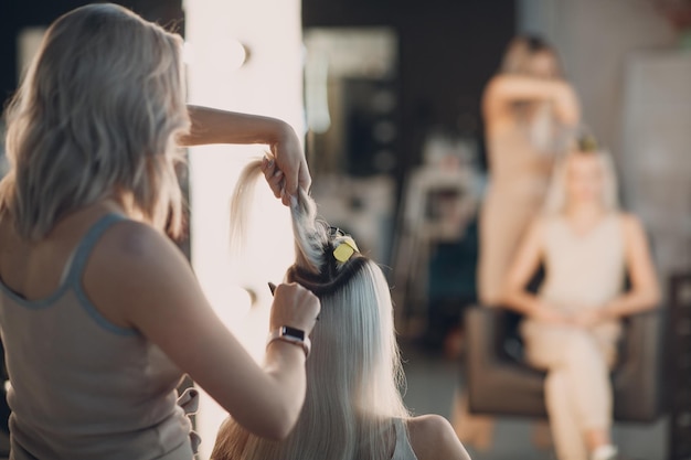 Foto femmina di parrucchiere che fa le estensioni dei capelli alla giovane donna con capelli biondi nell'estensione professionale dei capelli del salone di bellezza