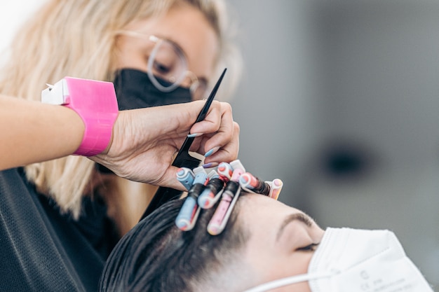 Parrucchiere che fissa i riccioli dei capelli di un uomo caucasico con maschera usando un pettine