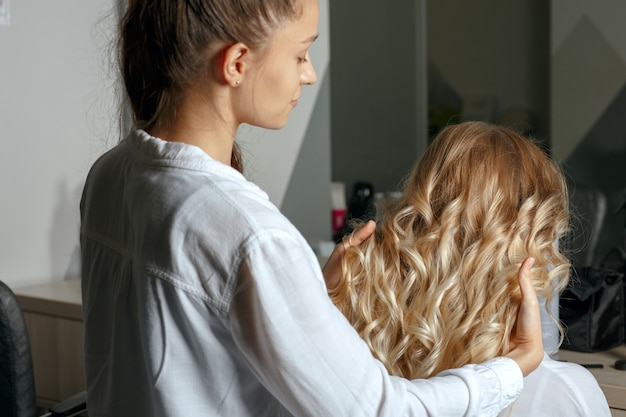 Hairdresser hands holding beautiful client's curls after dying and styling in a hair salon