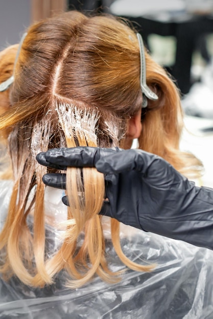 Photo a hairdresser is applying color to hair in black gloves. hair coloring in a beauty salon. beauty concept.
