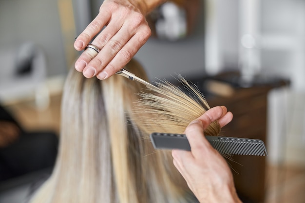 Hairdresser is choping hair of blonde woman is salon