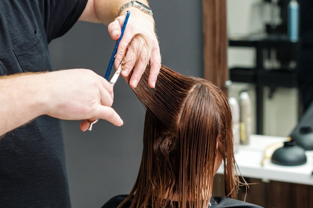 Hairdresser is cutting hair of young woman