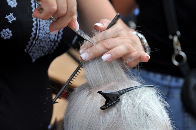 Hairdresser makes a haircut for an elderly woman.