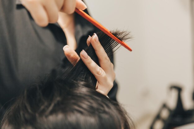 Hairdresser makes a haircut to a woman in the salon The hairdresser cuts wet hair combing with a comb client with short hair back view