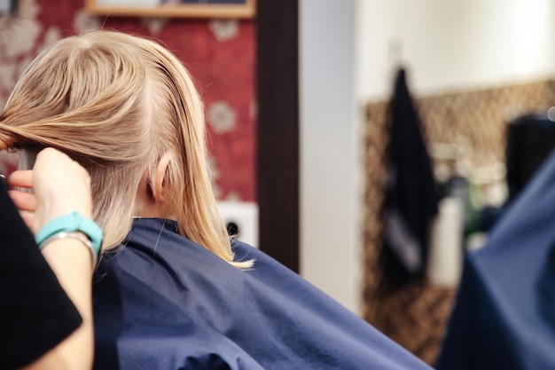 Hairdresser makes hairdo for little girl in barber shop Hair salon barber woman make fashionable pretty hairstyle