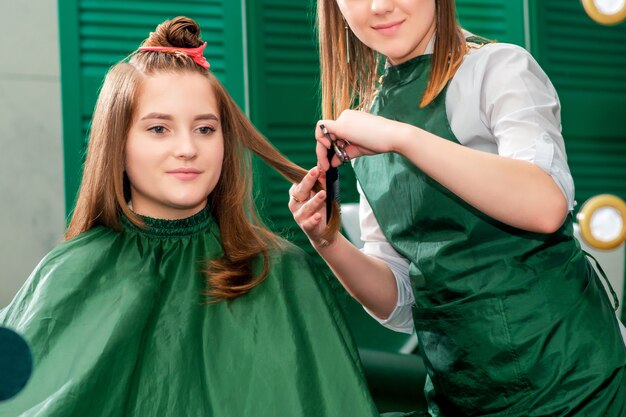 Hairdresser makes hairstyle for beautiful woman while looking in mirror reflection at beauty salon.