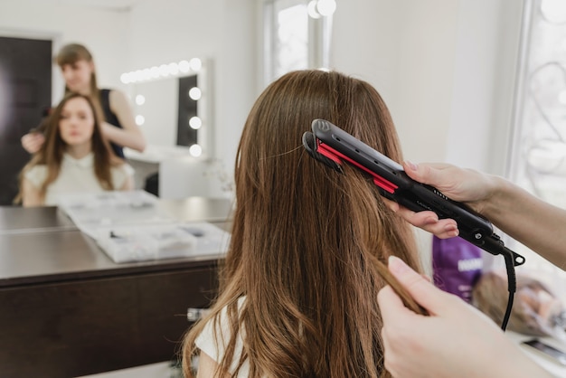 Un parrucchiere fa un'acconciatura per una ragazza in un salone di bellezza. liscia i capelli con un ferro da stiro