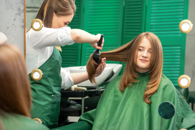 Hairdresser making hairstyling for the woman while combing with hairbrush, comb in a hair salon.