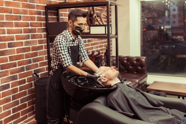 Hairdresser man washes client's head in vintage barbershop